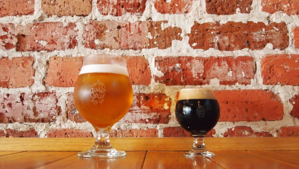 two glasses of beer sit in front of a brick wall on a table