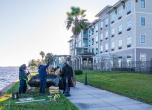 Three city workers installing purple martin pole bases with an apartment building in the background