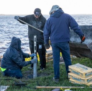 City workers measuring and aligning a purple martin pole base with bags of Quikrete concrete mix at the lake shore