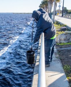 City worker filling a bucket with lake water from the Lake Monroe railing to mix concrete