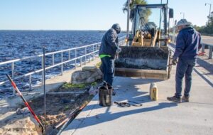 City workers using a bobcat skid steer to prepare a concrete base for a purple martin pole on the lakeside walkway