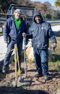 Two city workers smiling next to a newly installed purple martin pole base near Lake Monroe